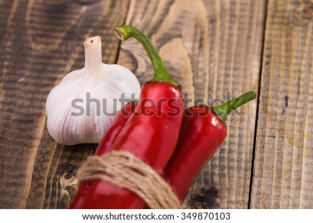 Closeup of appetizing organic aromatic spiciness ripe garlic and shining bright red chili peppers with green tails tied by brown rope healthy vegetarian diet on wooden background, horizontal picture