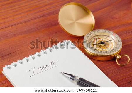 Closeup of notepad with handwritten word Trends and pen near compass on wooden board shallow depth of field