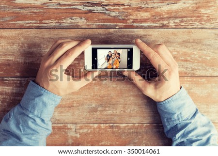 people, memory, relations and technology concept - close up of male hands holding smartphone with photo of happy friends on screen at table