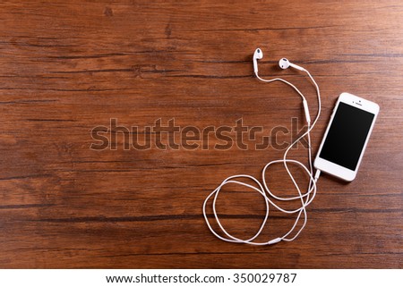White cellphone with headphones on varnished wooden background