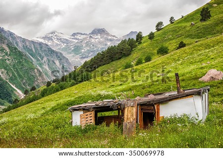 Poor old dilapidated abandoned house of the shepherd on a green meadow in the valley of the mountains, Elbrus region. Doors of house are opened