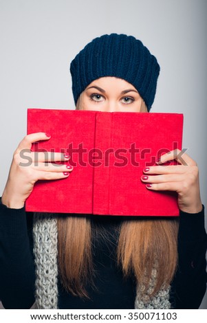 bright beautiful girl hiding behind the book, studio photo isolated on a gray background