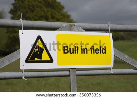 Bull in field warning sign attached to farm gate England UK
