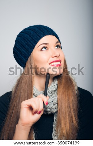 bright beautiful girl thinking with a pen, Christmas and New Year concept, studio photo isolated on a gray background