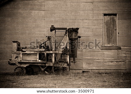 an old baler in front of a barn on the farm in sepia