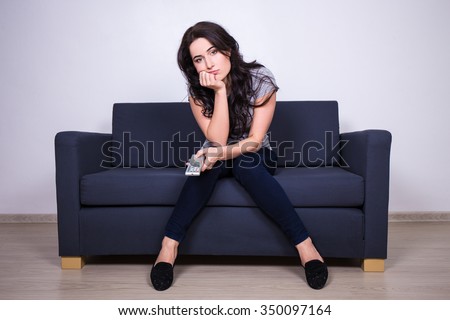 young bored woman sitting on sofa and watching tv at home