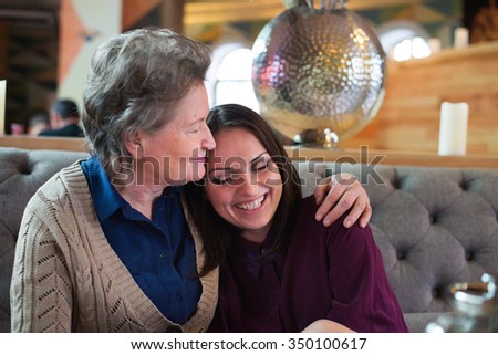 senior woman kisses her daughter at the cafe