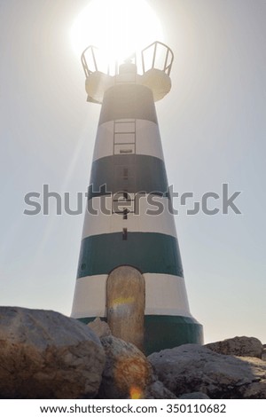 Picture of amazing lighthouse on blue sky background with brightly shining sun on top of lighthouse 