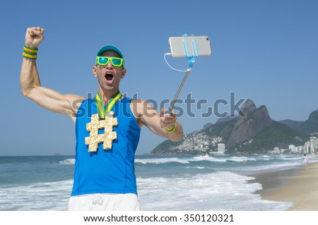 Hashtag gold medal athlete punching the air as he poses for a picture with his mobile phone on a selfie stick on Ipanema Beach in Rio de Janeiro, Brazil