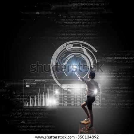 Back view of businesswoman standing on chair and reaching infographs on wall
