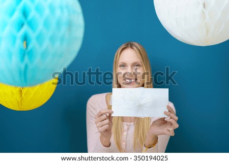 Pretty Woman inside a Studio with Hanging Honeycomb Balls, Holding White Present and Smiling at the Camera Against Blue Wall.