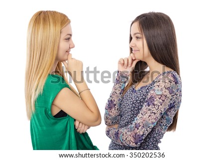 Closeup portrait of two teenage girls standing face to face with the hand on the chin over white background