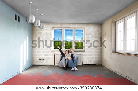 Happy Young Couple Sitting On Floor Looking Up While Dreaming Their New Home. Building in a developer