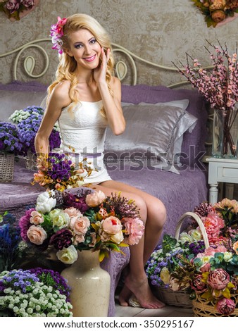 Beautiful Russian blonde girl sitting on a bed with a purple blanket , and around a lot of baskets with flowers