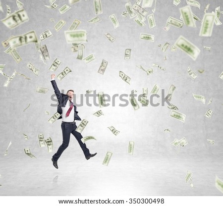 businessman in a suit jumping happily with his hand up, money falling from above, concept of success