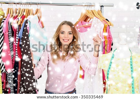 Beautiful young woman near rack with hangers over snow effect