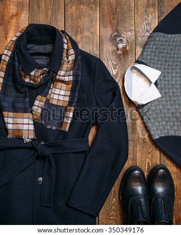 Classic men's wool coat with a warm scarf, sweater, shirt and leather shoes. A collection of warm winter classic men's clothing for the businessman. vertical photo on a wooden background.