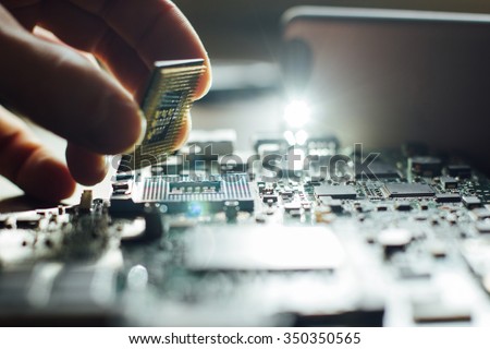 Technician plug in CPU microprocessor to motherboard socket. Workshop background Royalty-Free Stock Photo #350350565