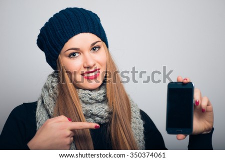 Bright girl points to the phone with your finger, winter concept, studio photo isolated on a gray background