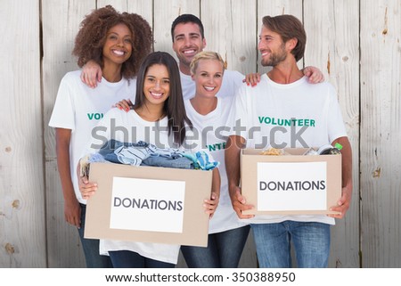 Happy group of volunteers holding clothes donation boxes against wooden background