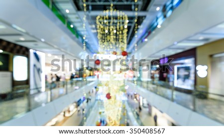 Blurred background of a modern shopping mall in Asia with beautiful Christmas decoration and people in motion. Shallow and selective focus. Xmas, New Year holidays abstract bokeh background. Panoramic