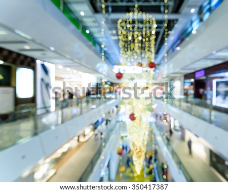 Blurred background of a modern shopping mall in Asia with beautiful Christmas decoration and people in motion. Shallow and selective focus. Xmas, New Year holidays abstract bokeh background