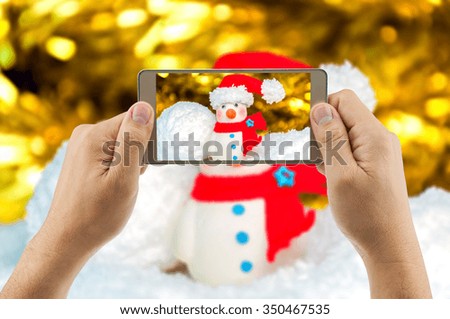 Man using mobile phone taking picture of snowman with blurred background. Celebrating  Christmas & New year festival.