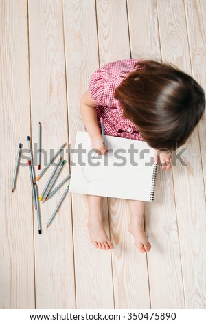 Unrecognizable child learns to draw with colored pencils. Girl sitting on the wooden floor and draw simple drawings.