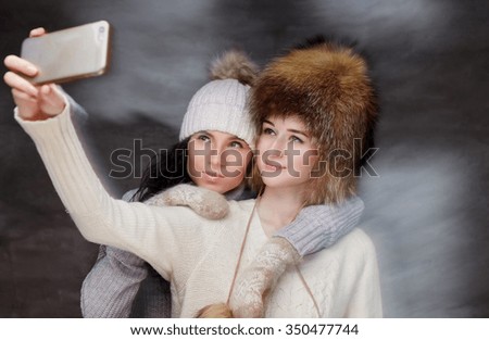 Two women in fur winter hats looking at smartphone.