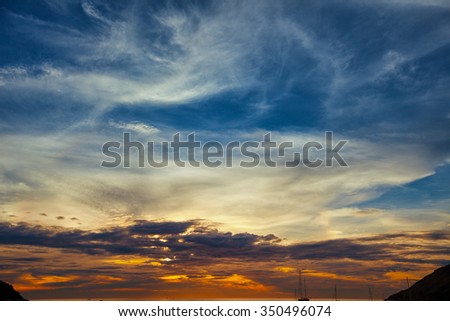 Sunset sky, lit in colors of blue, orange, lavender and gray, stretched out over the horizon of a tropical seascape.