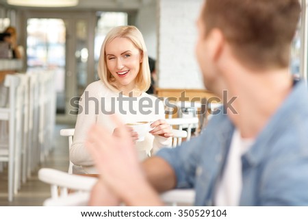 Time to flirt. Beautiful smiling young woman drinking coffee in the cafe and winking at handsome man while flirting with him Royalty-Free Stock Photo #350529104