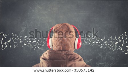 Teenager standing in front of a blackboard with musical notes drawn and listening to music on headphones