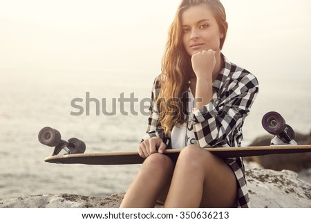 Beautiful and fashion young woman posing at the sunset with a skateboard 