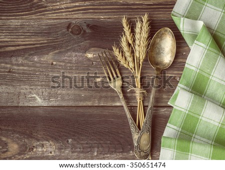 Vintage toned picture of the fork and spoon with the ears of wheat lying at the old table.