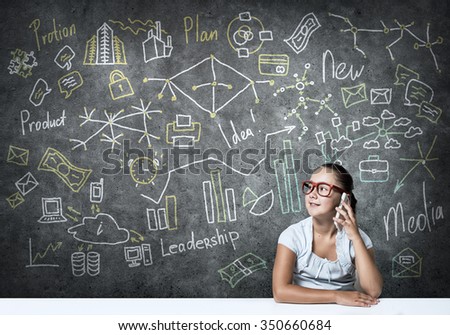 School girl in red glasses sitting at table talking mobile phone