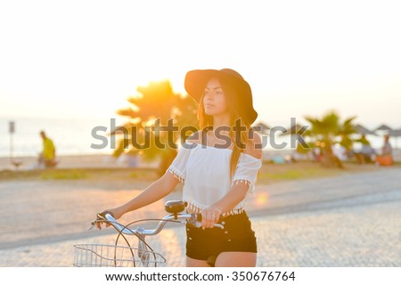 Lens flare photo of amazing lady wearing black floppy hat biking in sun flare on seaside background 