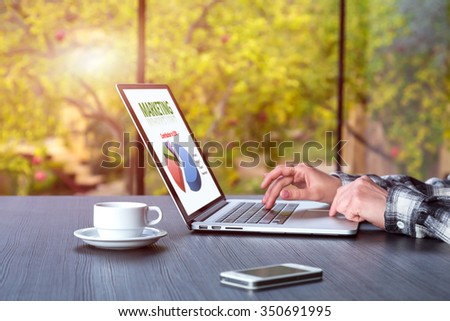 Person working on Computer with Telephone Coffee Mug on black wooden Table large Windows and green Garden View on Background