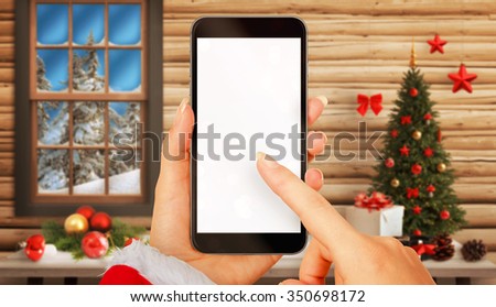 Woman with smart phone in hands in Christmas time. Device with white screen for mockup. Christmas tree, gifts, decorations in background. 