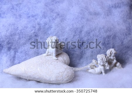 Closeup of beautiful soulful figurine composition of cupid angels for valentine day or christmas with small pillow in shape of heart lying on white wadding decorating snow, horizontal picture