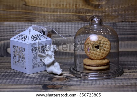 Closeup of beautiful cupid angel decorative figurine near white paper greeting valentine box and red hanging clothes-peg with round cookie under glass flask on wooden background, horizontal picture