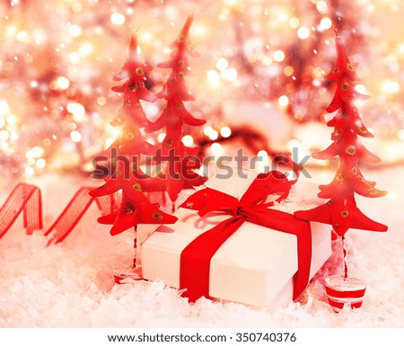 Beautiful festive still life, little gift box lying between red decorated Christmas trees, stylish Xmas decoration