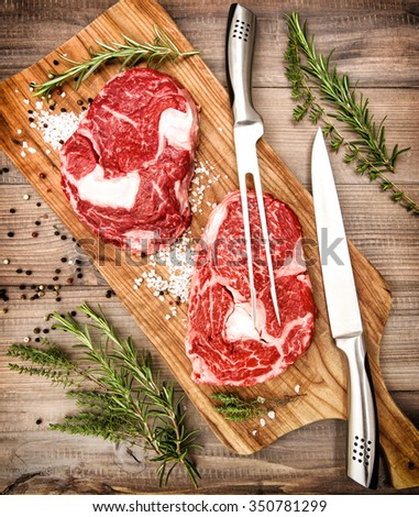 Raw fresh meat Ribeye Steak with herbs and spices on wooden desk. Vintage style toned picture