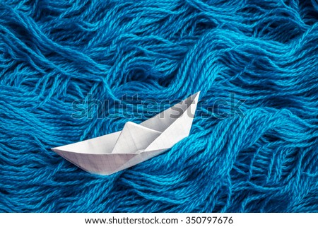 Cute white of origami boat floats on the sea waves of woolen yarn