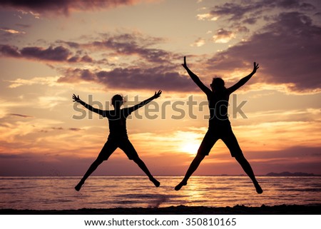 Mother and daughter jumping on the beach at the sunset time Concept of happy friendly family.