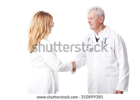 Portrait of medical standing against white background. Senior doctor and confident female doctor shaking hands. 