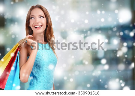 Beautiful young woman with bags in shopping center over snow effect