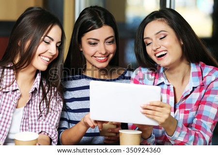 Three smiling friends with coffee looking at tablet