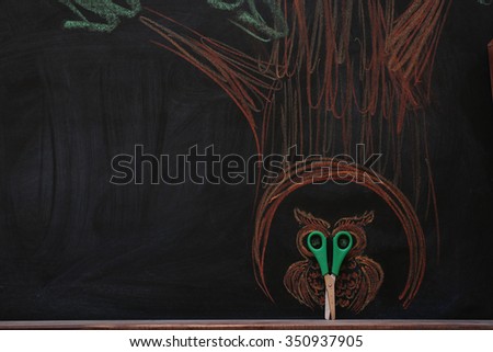 Concept of owl in hollow tree with scissors and chalk on black background