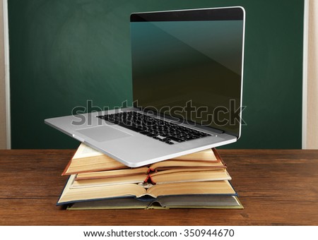 Stack of books with laptop on table in classroom