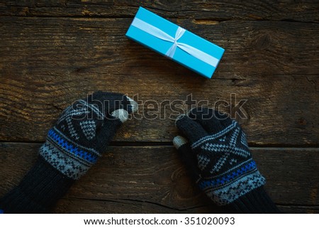 Hands in winter gloves with christmas gift box on wooden background